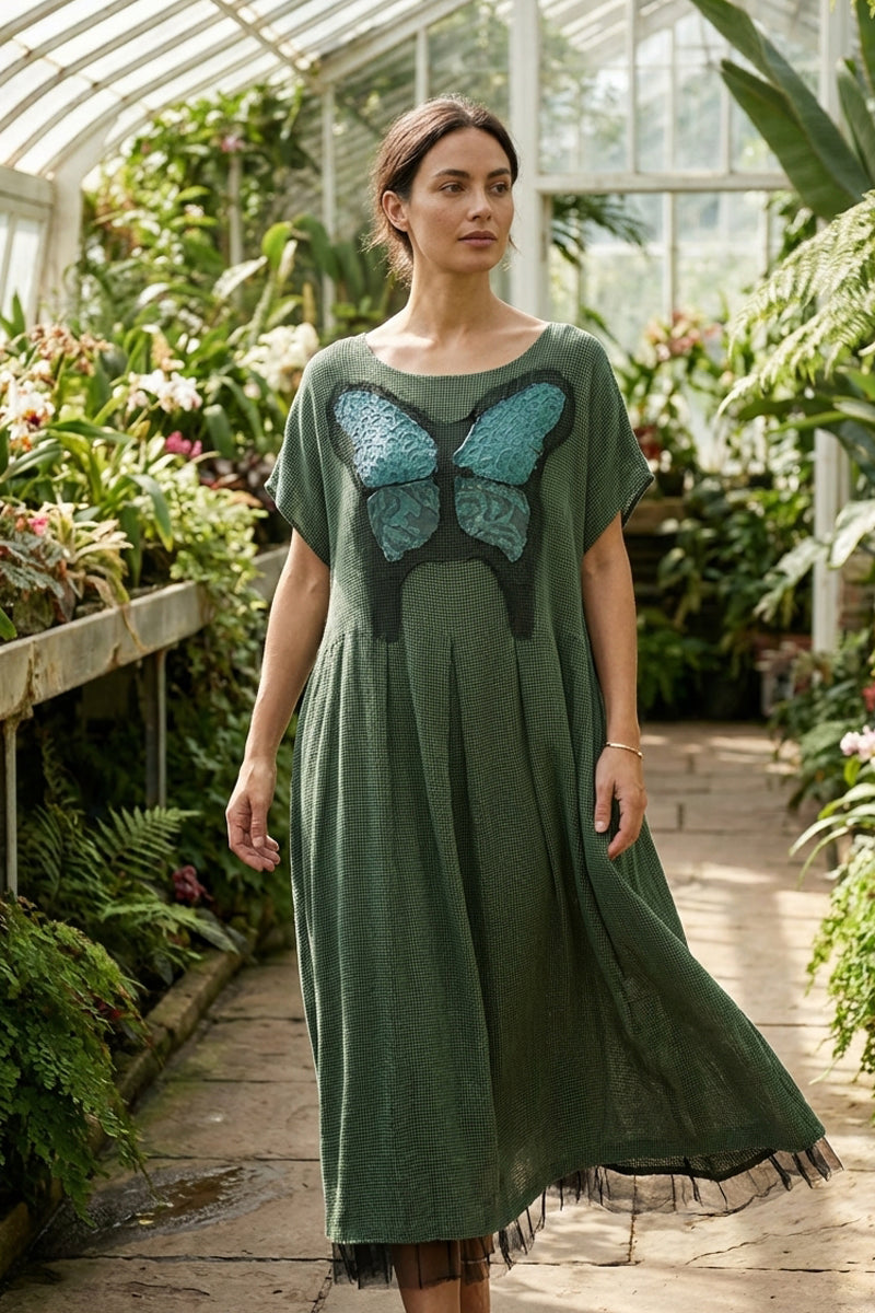 Woman wearing a green dress with a butterfly design in a greenhouse